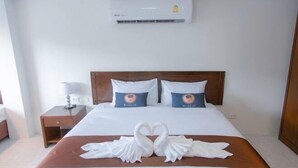 A hotel room with a bed, two pillows, a nightstand, a lamp, and a wall-mounted air conditioner. - RoomQuest the Beach Kalim Patong (Phuket)