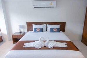 Una habitación de hotel con una cama, dos almohadas, una mesita de noche, una lámpara y aire acondicionado instalado en la pared.