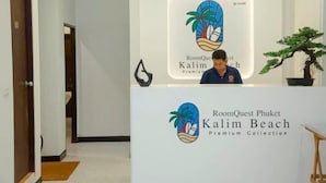 Un comptoir d’accueil orné du logo de RoomQuest Phuket Kalim Beach Premium Collection.