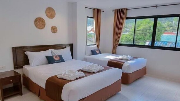 Une chambre d’hôtel avec deux lits, une table de chevet, une fenêtre avec des rideaux et une vue sur la verdure.