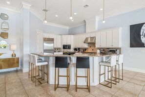 A modern kitchen with white cabinets, a central island with bar stools, stainless steel appliances, and pendant lighting. - The Family Fun House-TT350 (Kissimmee)