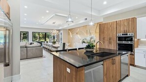 Une cuisine moderne dotée d’un îlot central, de meubles en bois, d’appareils électroménagers en acier inoxydable, de luminaires suspendus et donnant sur un coin repas.