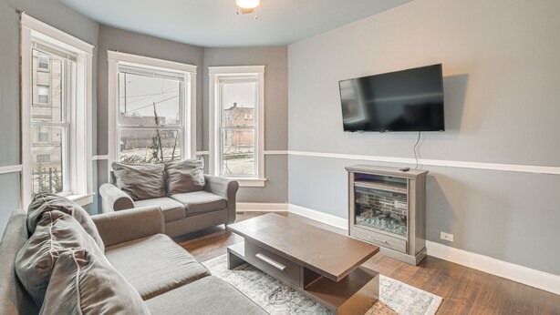 Ein Wohnzimmer mit grauem Sofa, Couchtisch, Kamin und flachbildfernseher an der Wand.