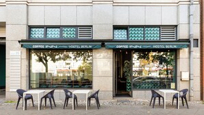 A hostel with a green awning and the name 'Coffee Inn Hostel Berlin' displayed. There are four tables and chairs outside the entrance. - Coffee Inn Hostel Berlin (Berlin)