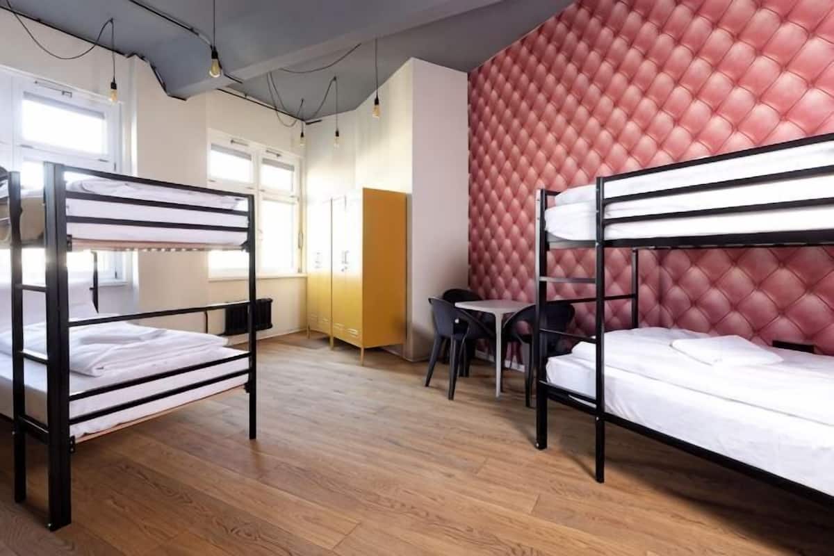 A dormitory room with bunk beds, a desk, and a red tufted wall.