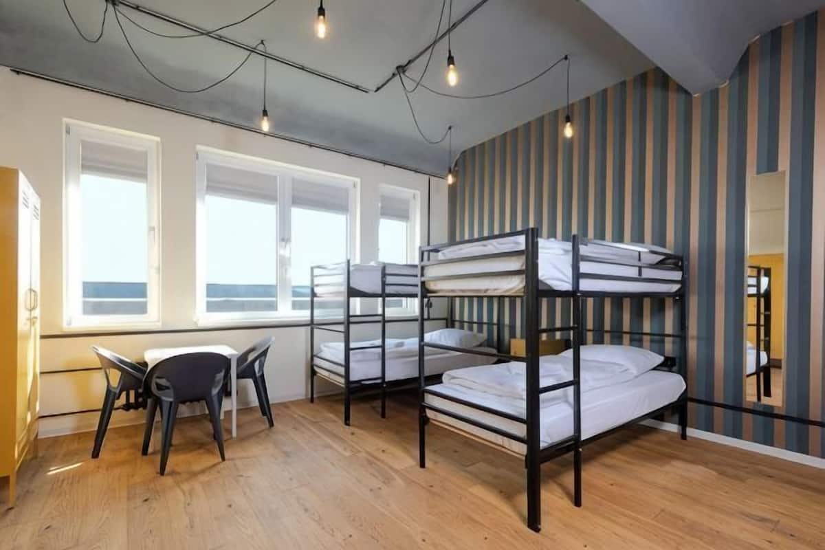 A dormitory room with bunk beds, a desk, and a chair.