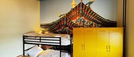 Une chambre de dortoir avec des lits superposés, une fresque représentant un bâtiment traditionnel et des casiers jaunes.