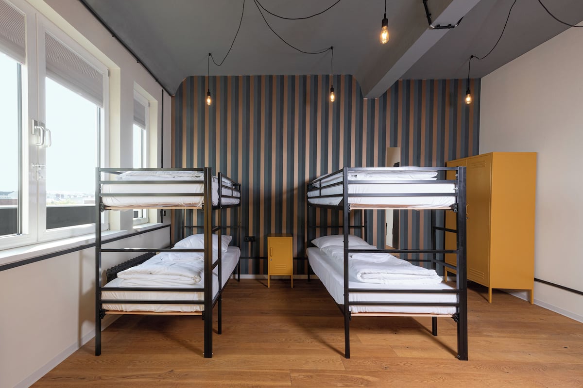 A dormitory room with bunk beds, wooden flooring, and a striped wall.