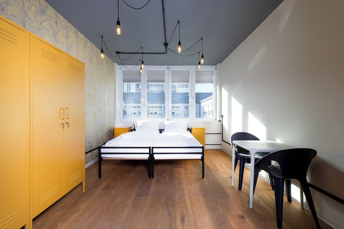 A bedroom with a bed, yellow wardrobe, and a window with a view of buildings.