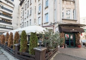A building with a restaurant named "Trattoria Verde" on the ground floor, featuring outdoor seating with potted plants and a wooden fence. - Highline Downtown Aparthotel (Bucharest)