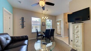A living room with a glass coffee table, a leather couch, a ceiling fan, a dining area with chairs, a TV mounted on the wall, and a cabinet with decorative items. - Apartment for 4 guests (Sarasota)