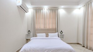 A modern bedroom with a large bed, white bedding, a headboard, bedside tables with lamps, and a window with sheer curtains. - Styling 5 BR Duplex Apartment (First 6th of October)