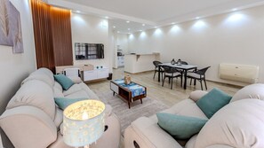 A modern living room with a sofa set, a coffee table, and a dining area with chairs and a table. - Styling 5 BR Duplex Apartment (First 6th of October)