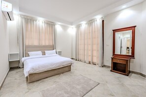 Quarto de hotel com uma cama grande, uma mesa de cabeceira de madeira, um espelho e um ar condicionado fixado na parede.