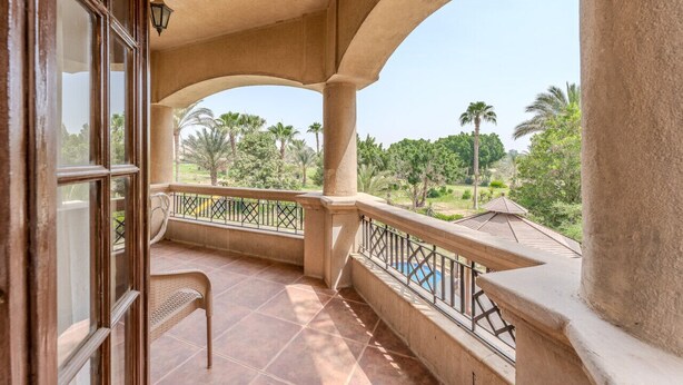 A balcony with a view of palm trees and a pool. - Styling 5 BR Duplex Apartment (First 6th of October)