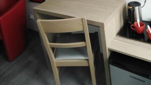 Una habitación compacta con un escritorio de madera, una silla roja, una lámpara de pie roja y un lavavajillas negro.