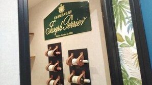 Una pared con un letrero que dice "CHAMPAGNE Joseph Perrier" y una estantería llena de botellas.