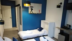 Habitación de hotel con dos camas, un escritorio, una silla, un refrigerador pequeño y un cuadro en la pared.