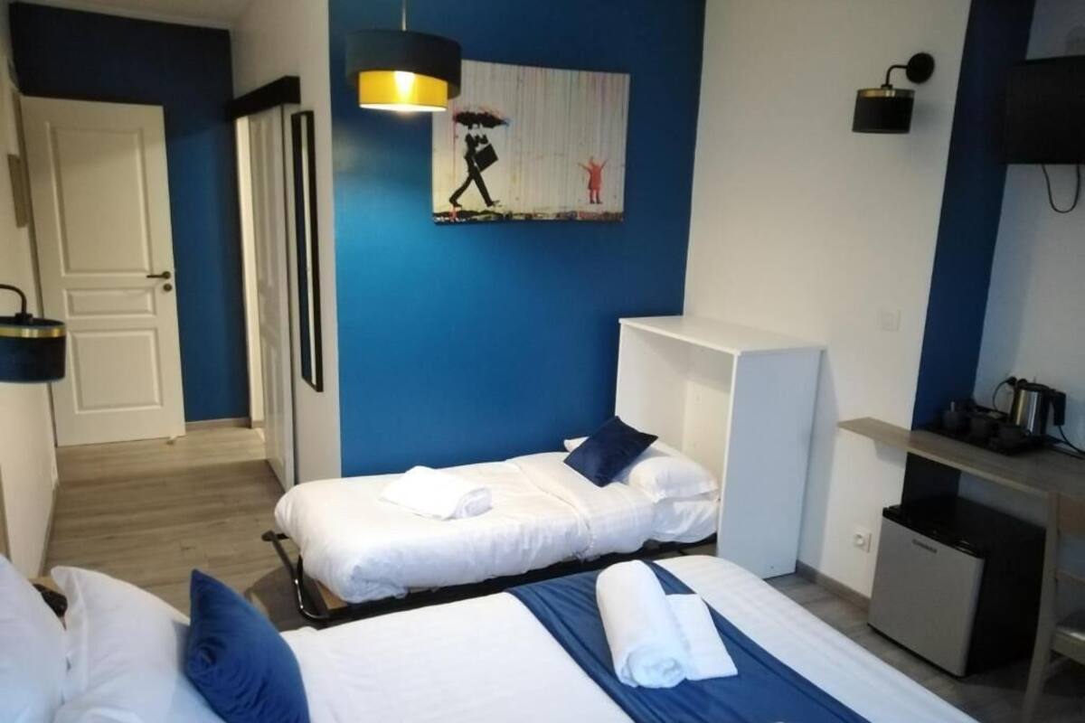Ein Hotelzimmer mit zwei Betten, einem Schreibtisch, einem Stuhl, einer kleinen Minibar und einem Bild an der Wand.