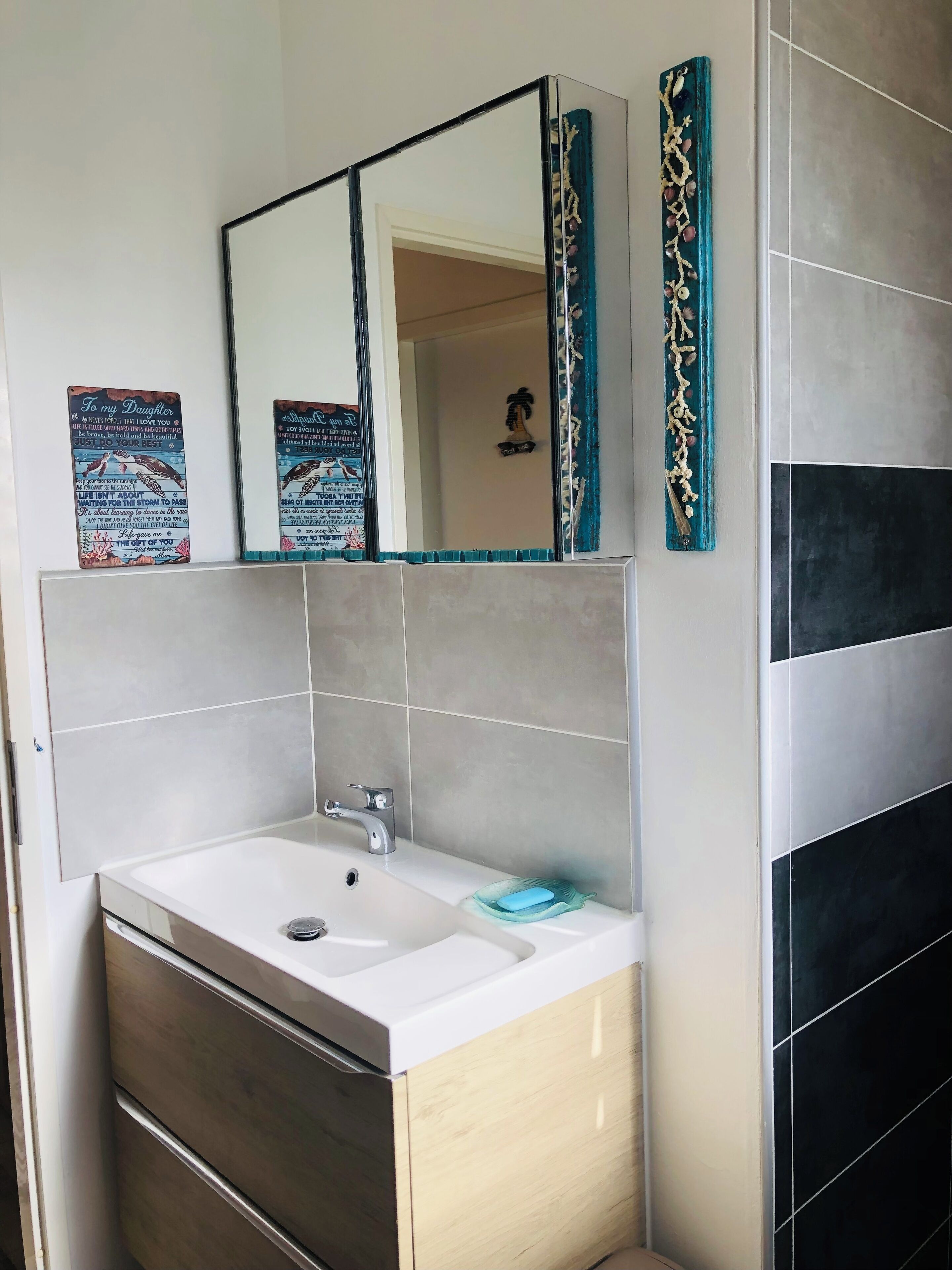 A bathroom with a white sink, a mirror, and a decorative piece above the mirror.