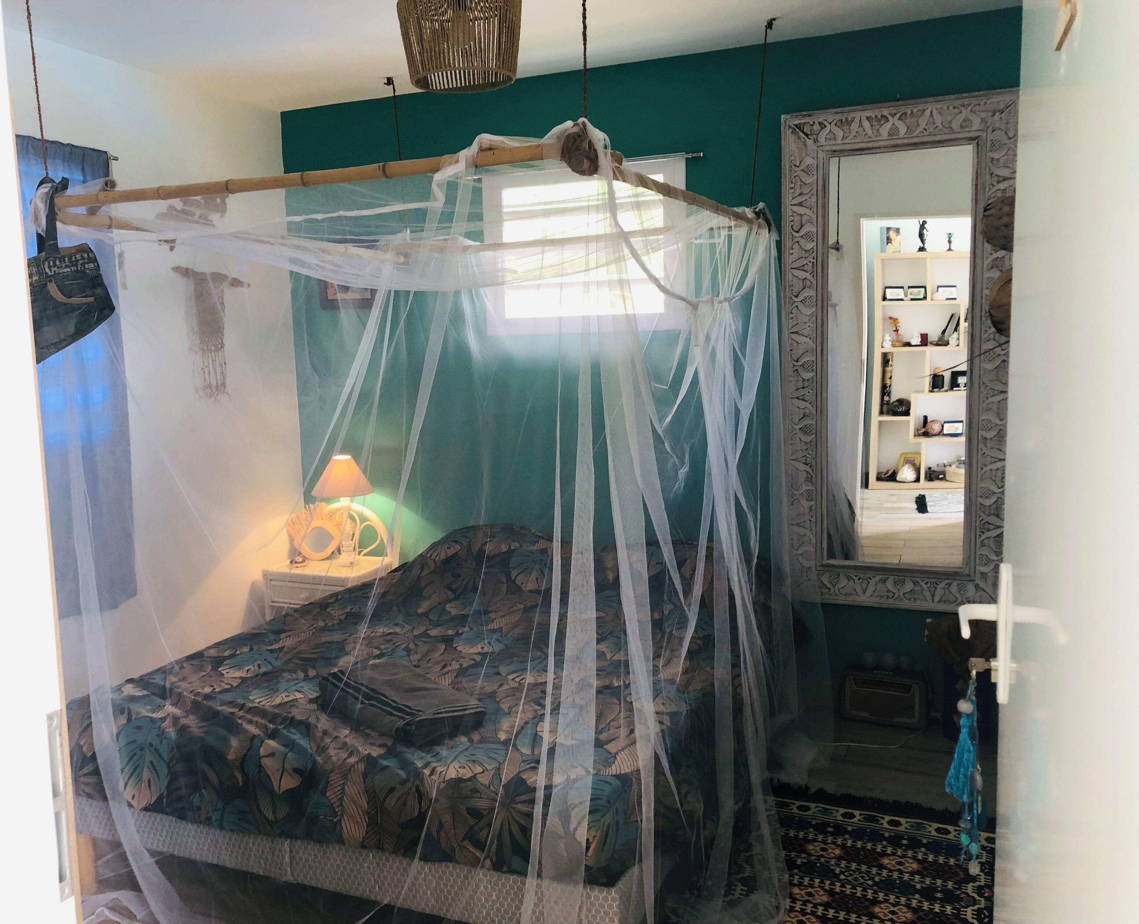 A bedroom with a bed under a mosquito net, a bedside lamp, a mirror, and a patterned rug.