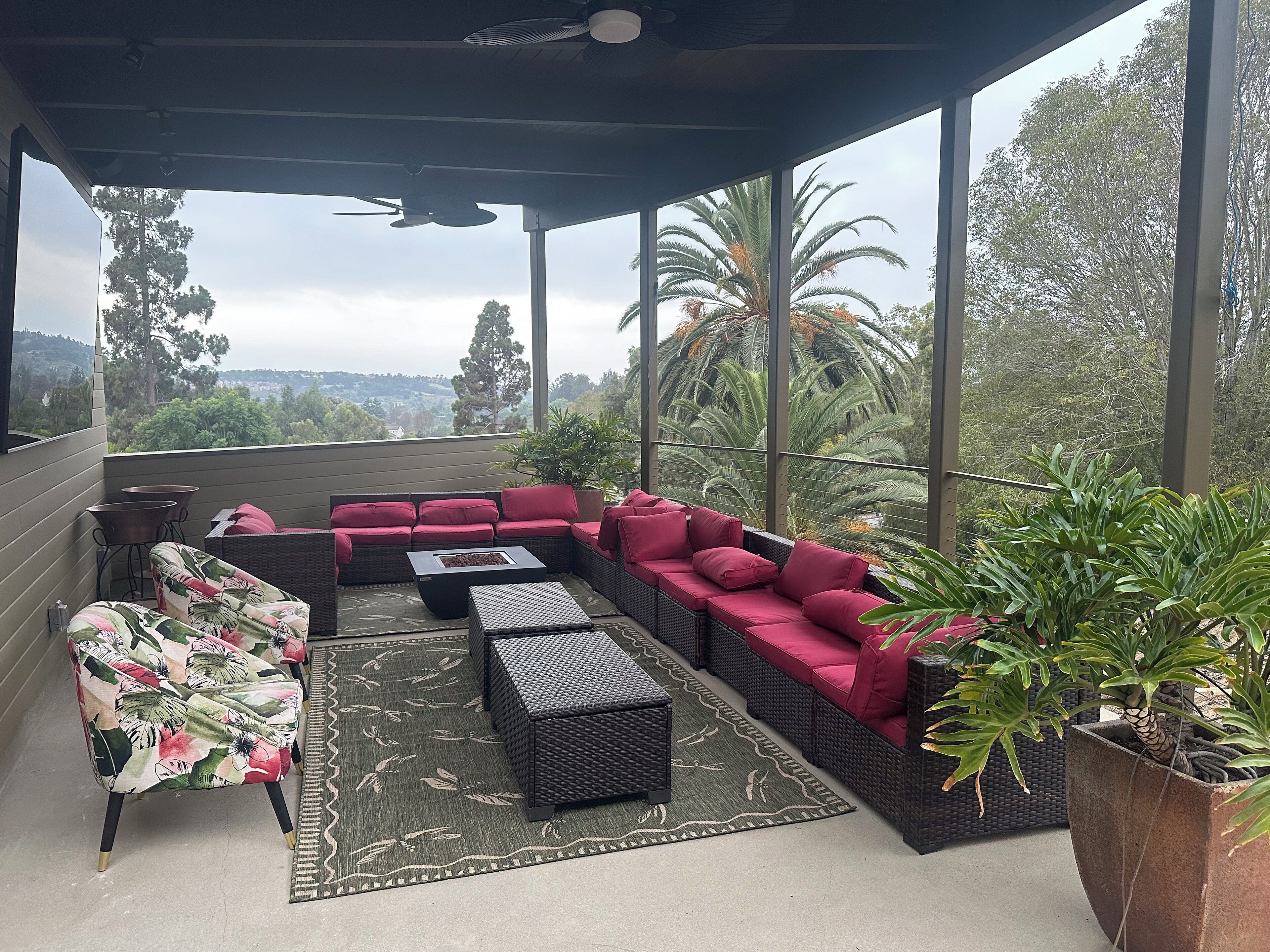 Un espace extérieur aménagé, abrité et doté de mobilier en osier et de coussins rouges, offrant une vue sur un paysage luxuriant.