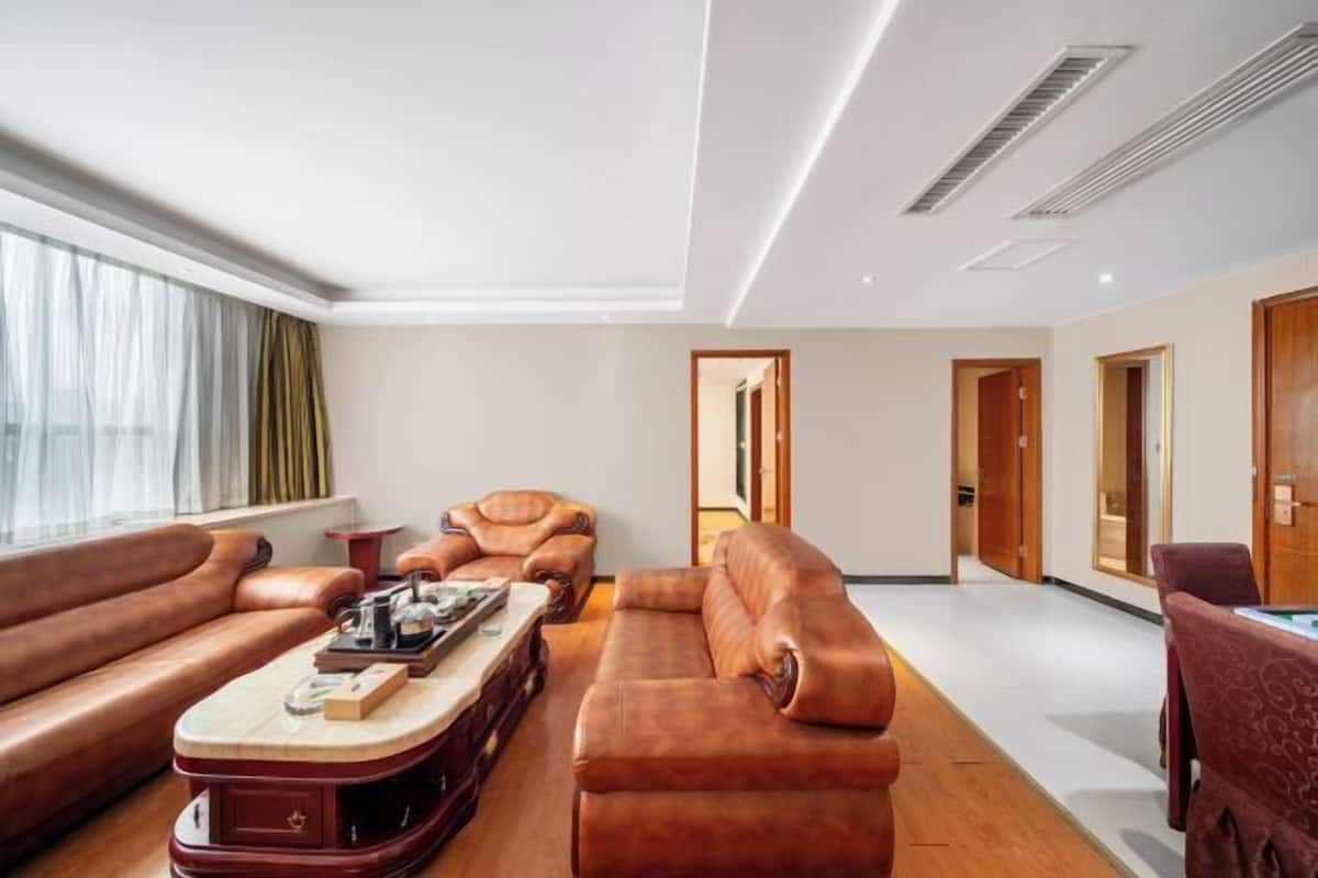 A modern living room with leather sofas, a coffee table, and a view of the city through large windows.