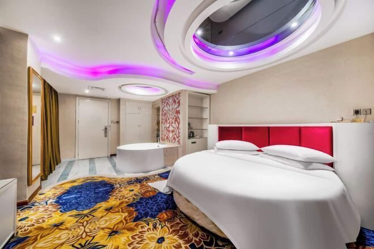A modern hotel room with a large bed, a round mirror, and a unique ceiling design with circular lighting.