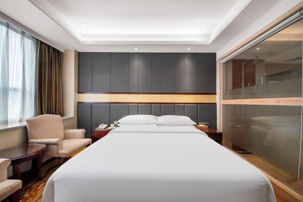 A hotel room with a large bed, a desk, a chair, a wardrobe, and a sliding door.