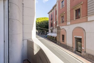 Una vista di strada con un edificio con facciata rossa, ingresso custodito e un cartello visibile.