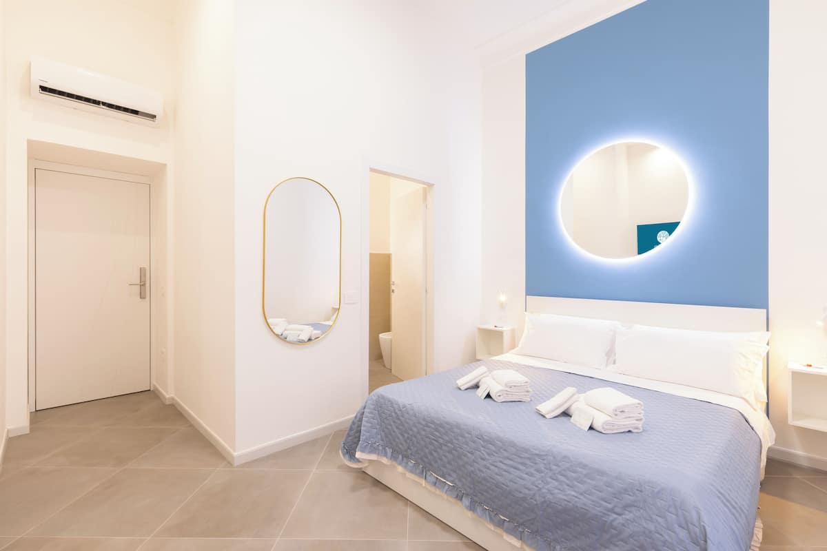 Una habitación de hotel moderna con una cama, un espejo redondo y una pared azul decorativa.