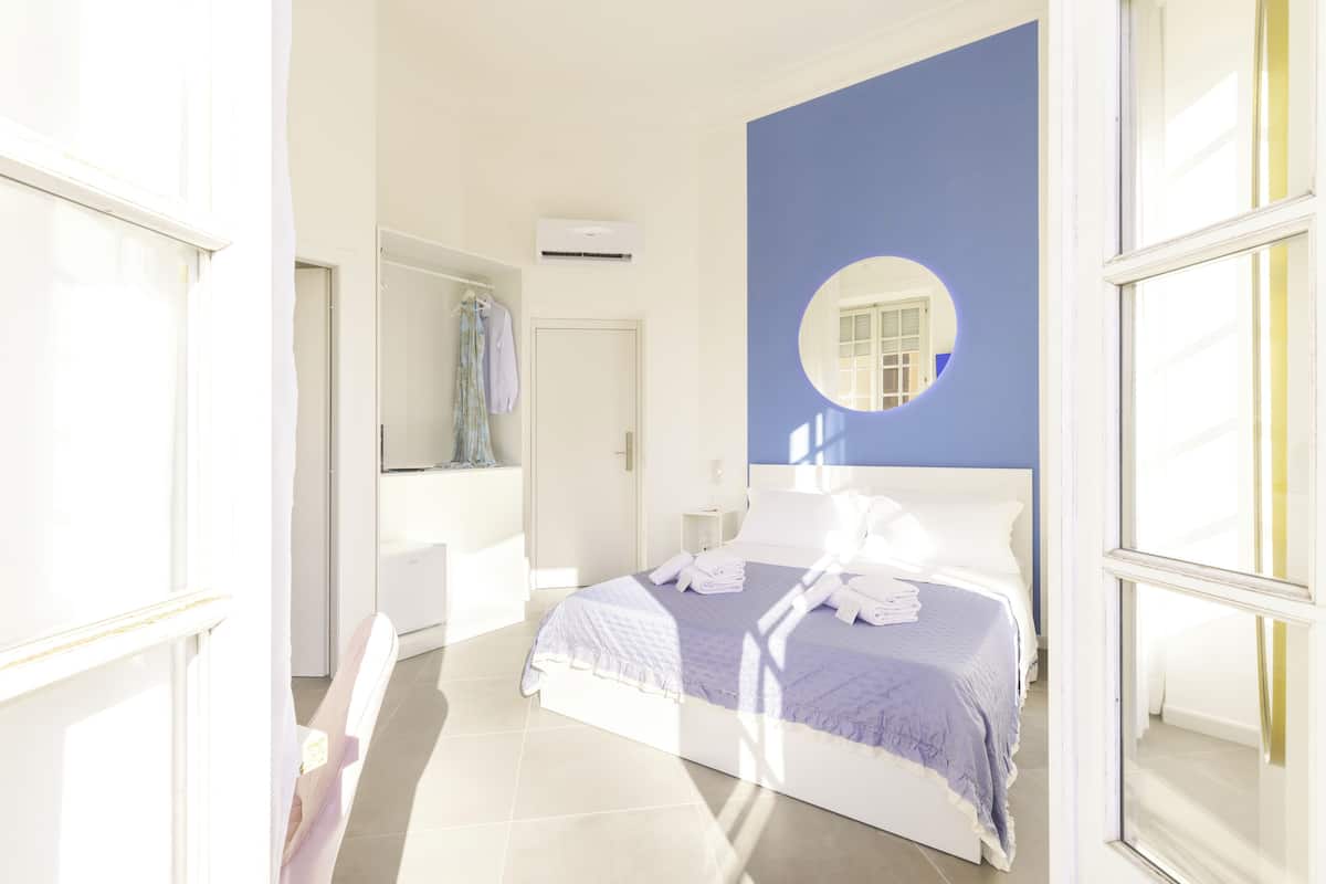 Un dormitorio luminoso con una cama grande, un espejo redondo y vistas al baño.