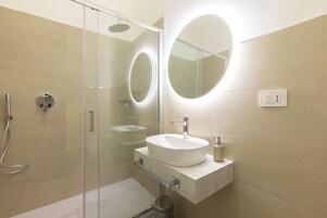 Un baño moderno con cabina de ducha de vidrio, un espejo redondo y un lavabo blanco con encimera.