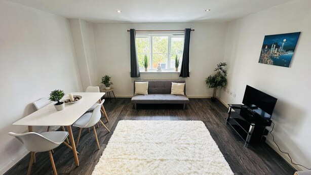 Ett modernt vardagsrum med en soffa, ett matbord, stolar, en vit matta, en tv och ett fönster med gardiner.