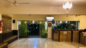 A hotel lobby with a reception desk, a fire extinguisher, a television screen, and a ceiling fan. - Wishotel Xpress 7 Eleven  (Indore)
