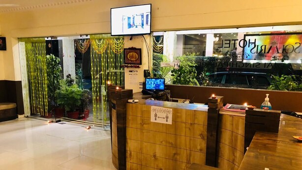 A hotel reception area with a wooden reception desk, a television screen, and a sign indicating social distancing measures. - Wishotel Xpress 7 Eleven  (Indore)