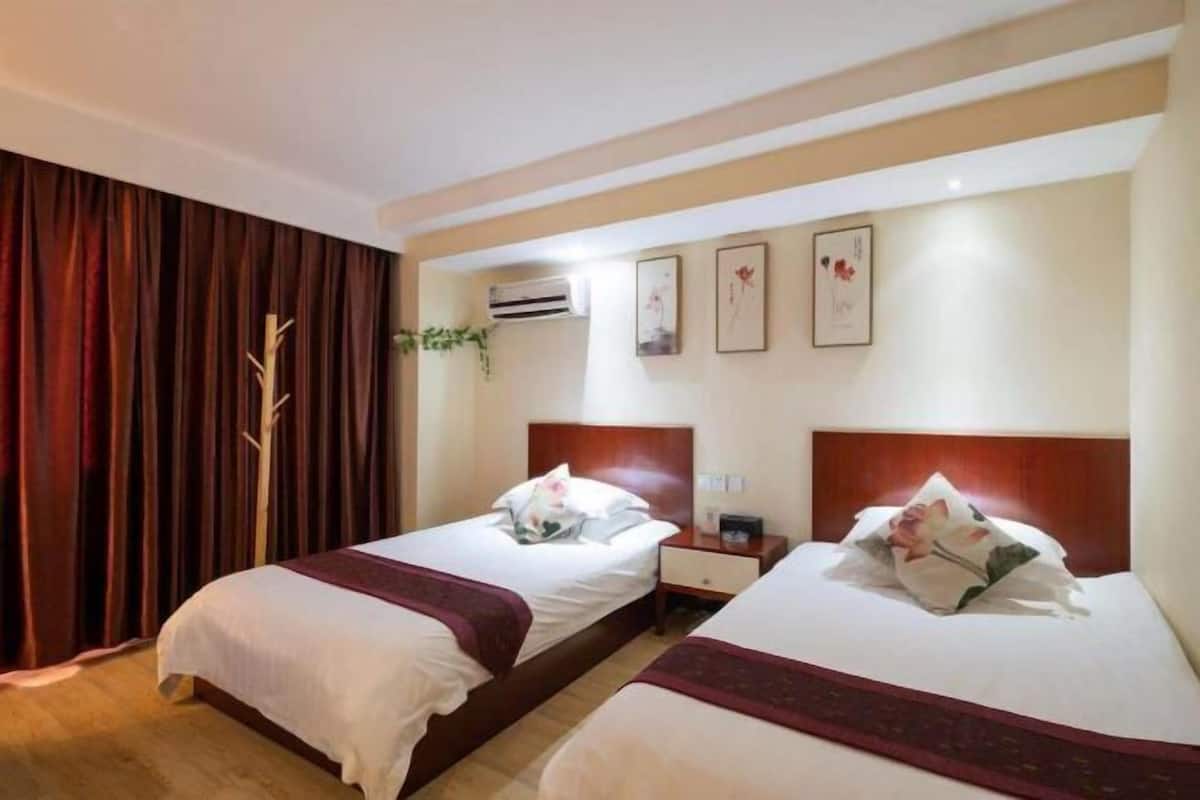 Hotelkamer met twee bedden, een houten hoofdbord, een nachtkastje, een airconditioner en een raam met gordijnen.