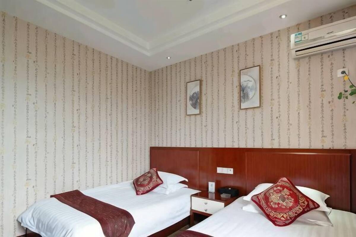 Een hotelkamer met twee bedden, een houten hoofdbord, een nachtkastje, een ingebouwde airconditioner en een lijst met een afbeelding.