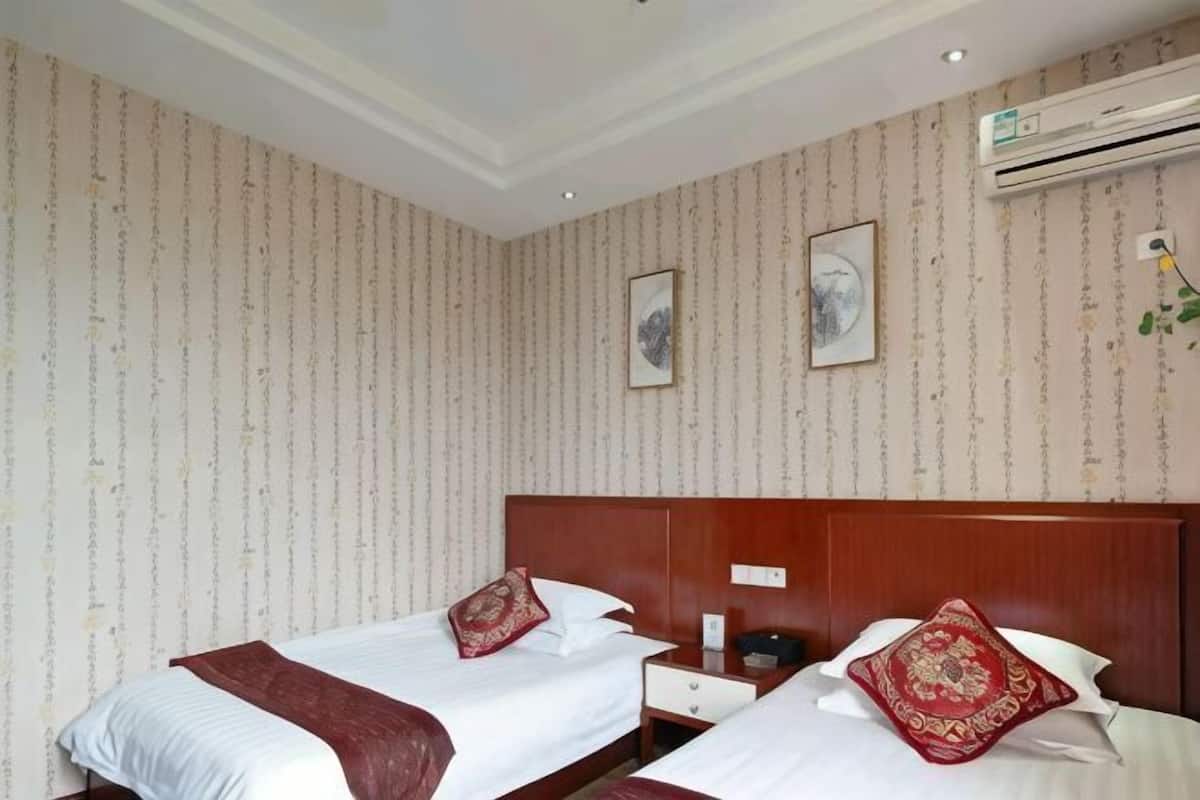 A hotel room with two beds, a wooden headboard, a nightstand, a wall-mounted air conditioner, and a framed picture.