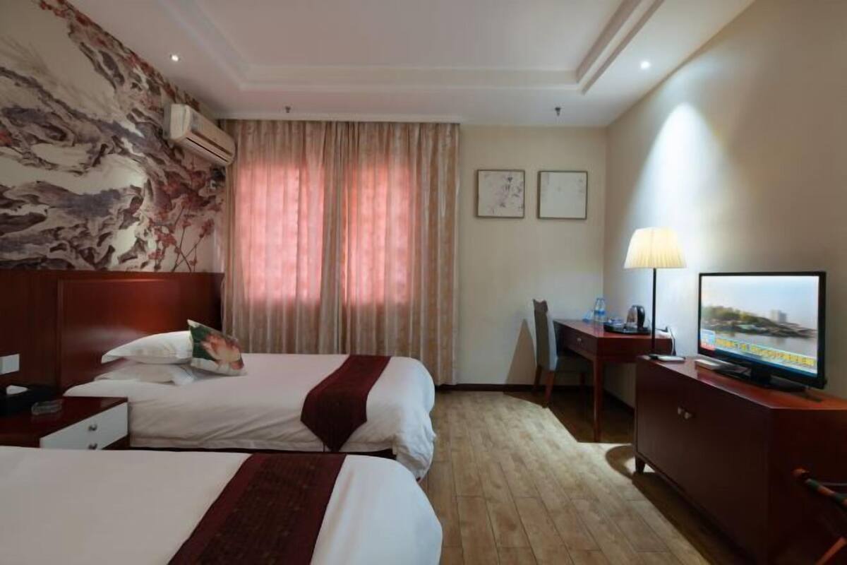 Hotelkamer met twee bedden, een bureau, een televisie en een groot raam met gordijnen.