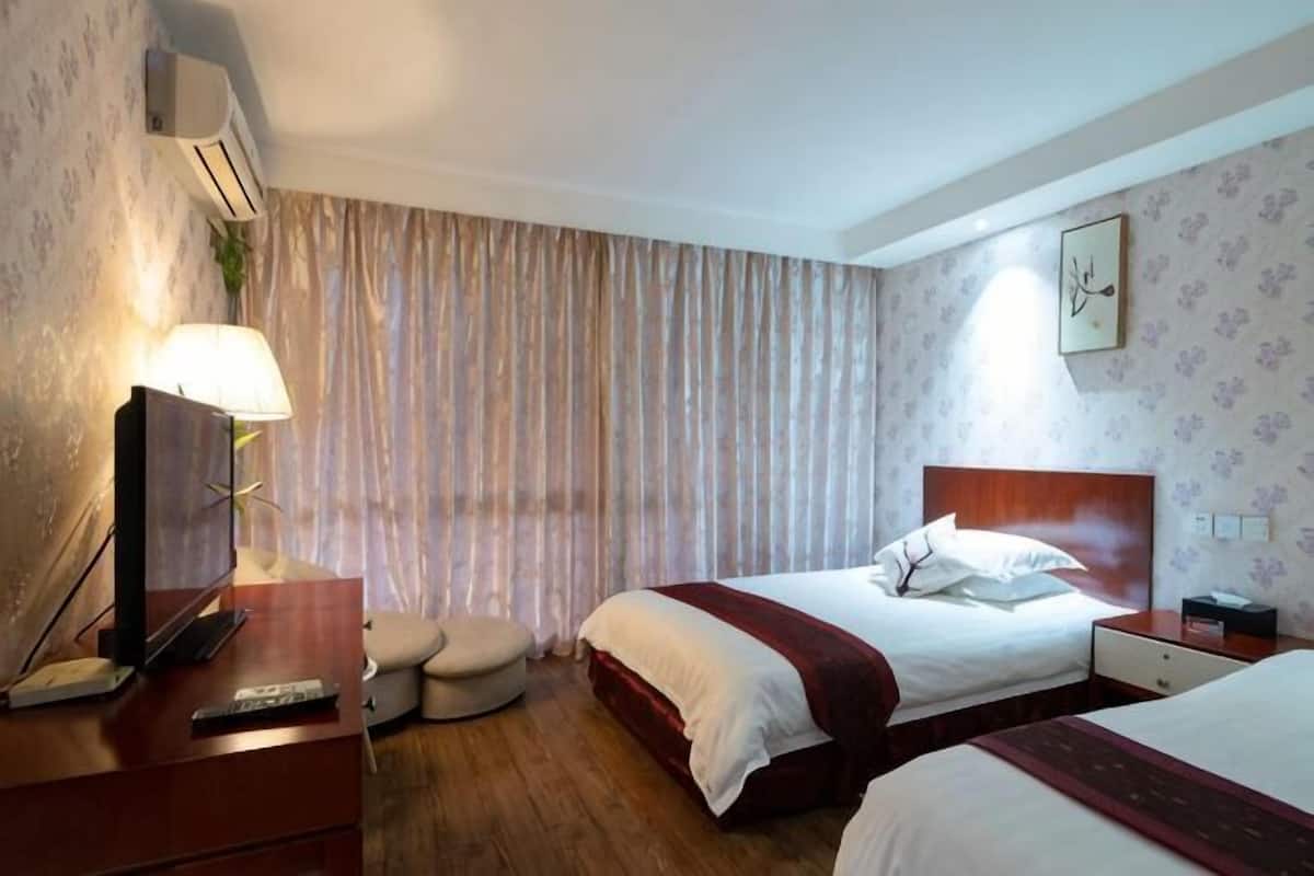 Een hotelkamer met twee bedden, een televisie, een lamp, een nachtkastje en een wandklok.