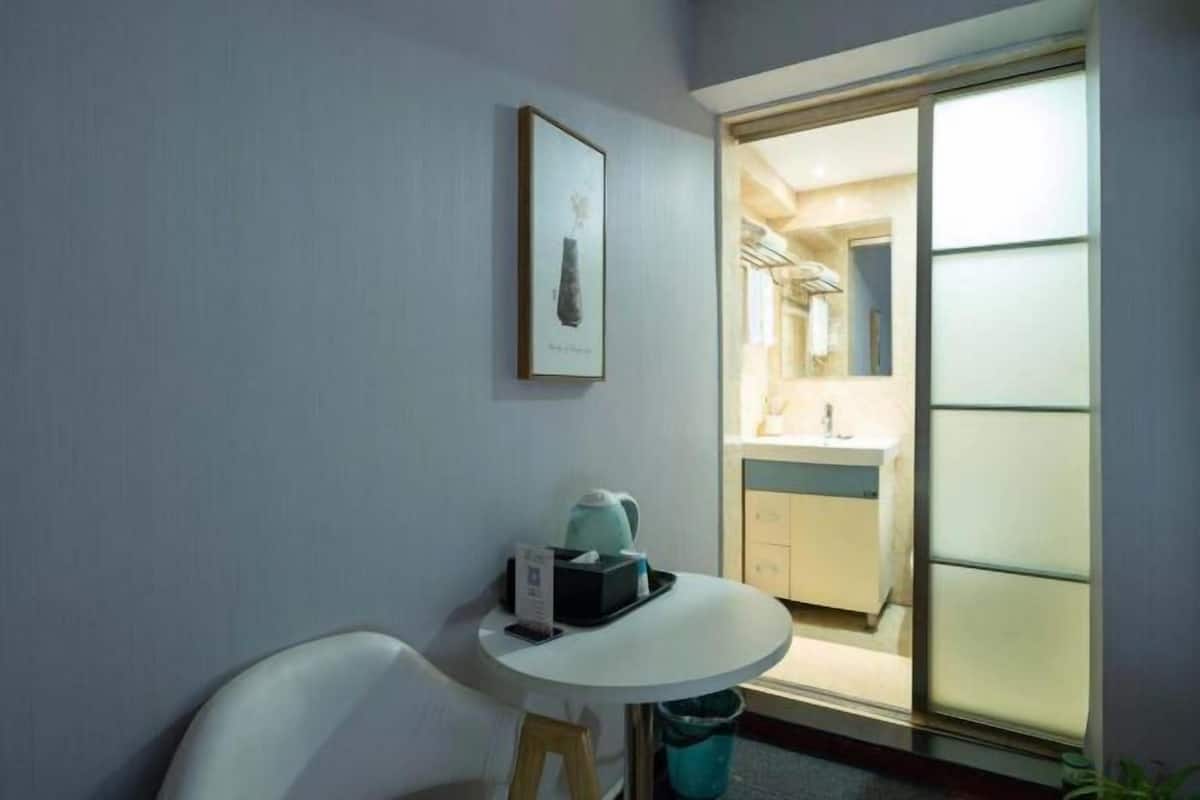 Een hotelkamer met een klein tafeltje, een stoel, een ingelijst beeld aan de muur en een schuifdeur naar een badkamer.