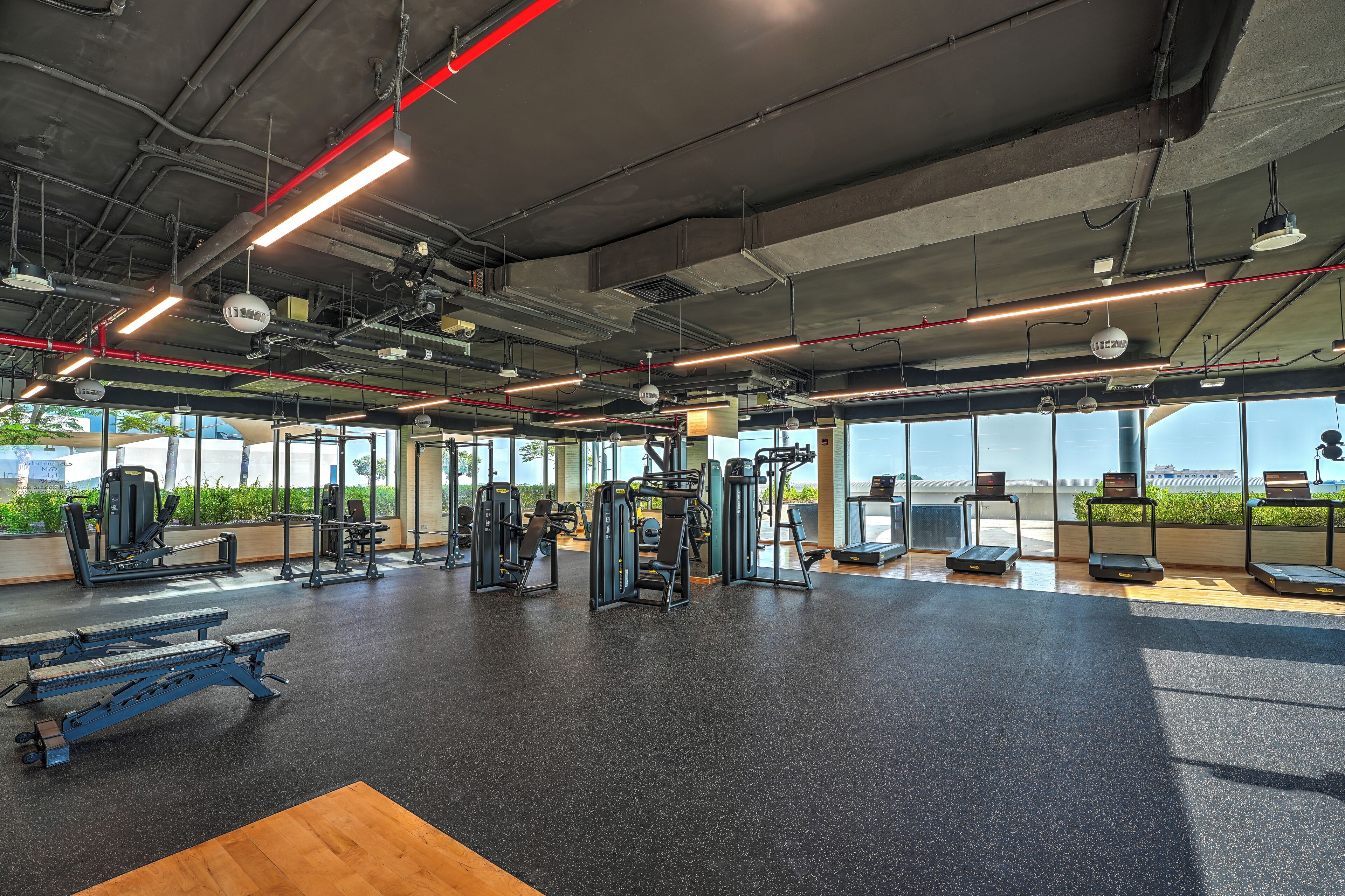 A gym with various exercise equipment, large windows, and a view of the outdoors.