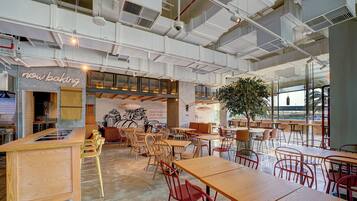 A modern cafe with exposed ceilings, wooden tables, and chairs, and a large window offering a view.