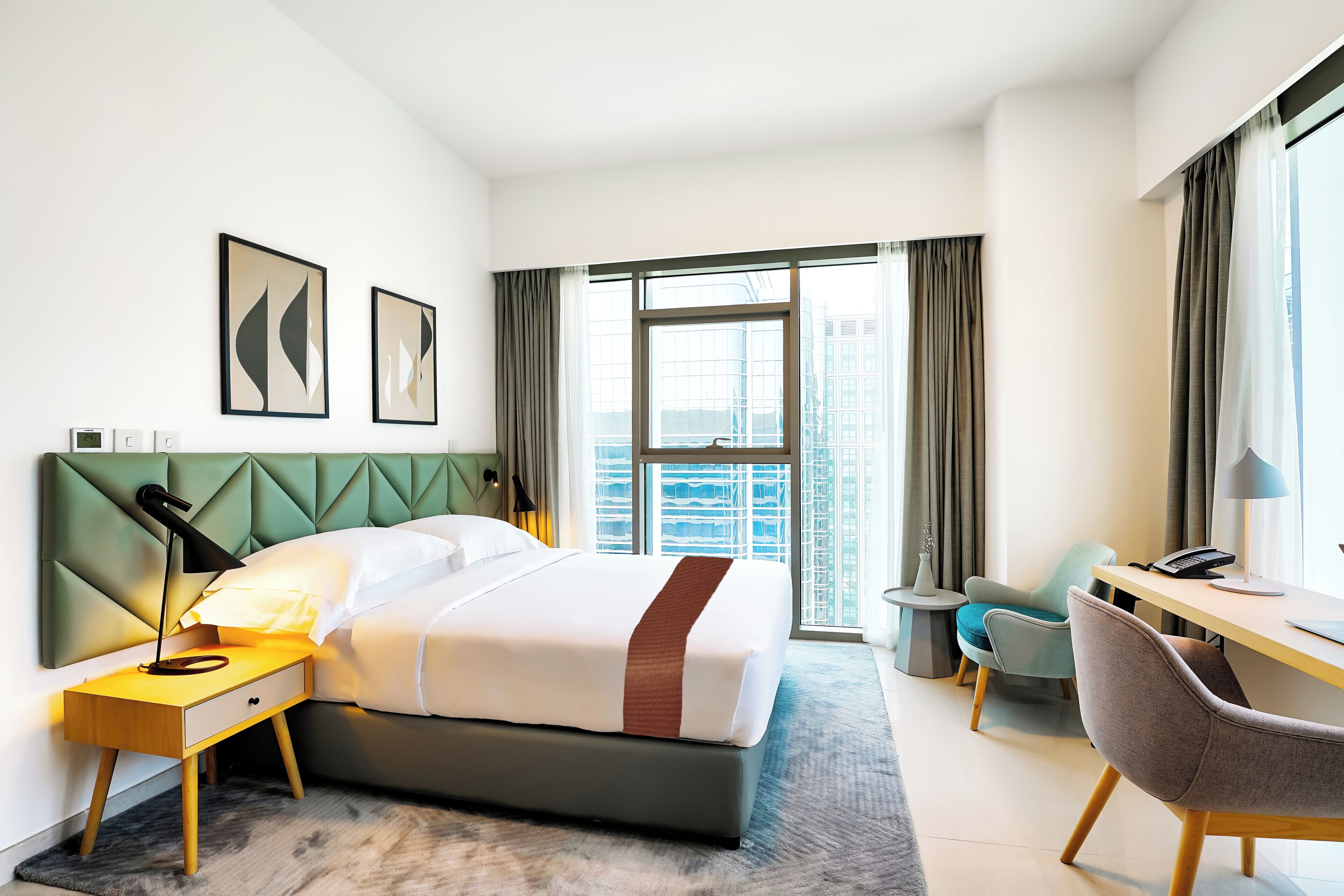 Une chambre d’hôtel moderne, dotée d’un grand lit, d’un bureau, d’une chaise et offrant une vue sur la ville.