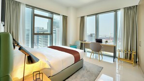 Een hotelkamer met een groot bed, een bureau en een stoel, met uitzicht op de stad door grote ramen.