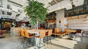 Een ruim café met een grote boom, hoge plafonds en modern meubilair.