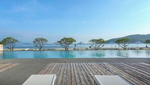 A wooden deck with lounge chairs overlooking a pool and beach.