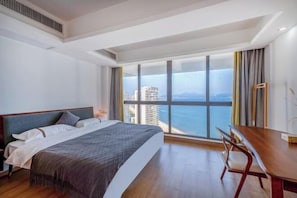 Habitación de hotel con una cama grande, un escritorio de madera y vistas al mar y a los edificios.