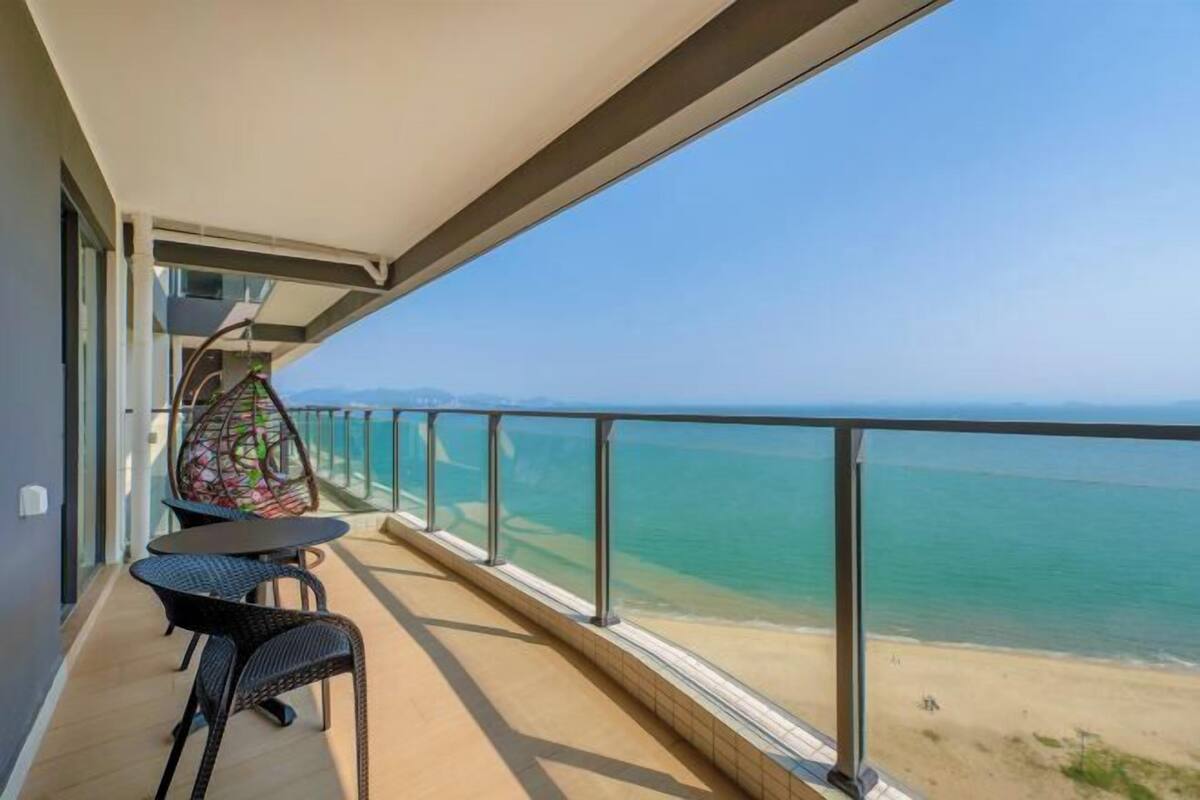 A balcony with a view of the sea, a table, two chairs, and a hanging chair.